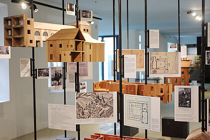 Dekoratives Ausstellungselement zur Geschichte des Volkskundemuseums am Paulustor mit alten Gebäudeplänen und Miniaturmodellen aus Holz.
