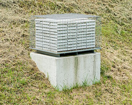 The sculpture denies access to 999 ingots made of the finest concrete. The neatly stacked ingots are surrounded by a grid. 