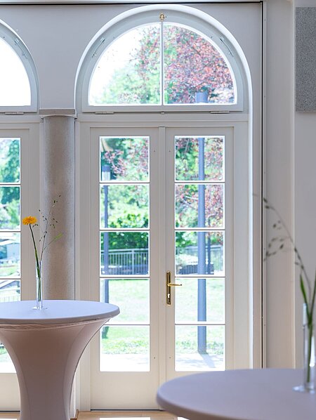 View through the double doors from the foyer into the fragrance garden. In the foyer are high tables with floral decorations.