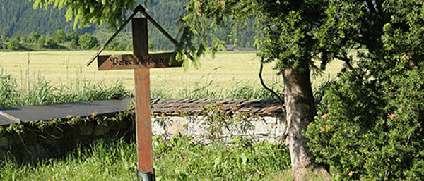 Einfaches Holzkreuz am Friedhofsrand unter Bäumen