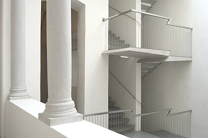 
White staircase with metal railing. There are two pillars in the foreground