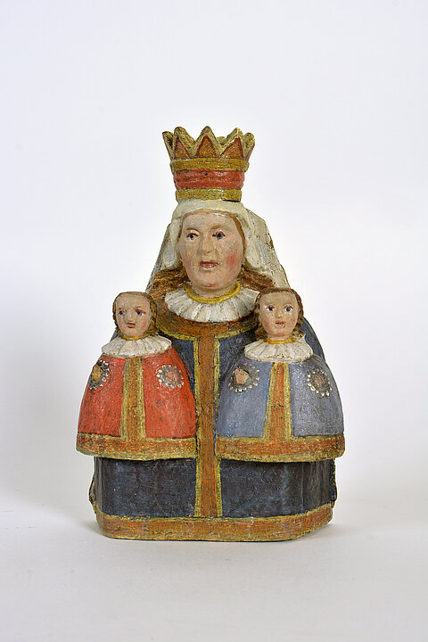 Wooden figure of a woman with a crown who has a small child on each side. The figure is painted. One child has a blue coat, another has a red coat.