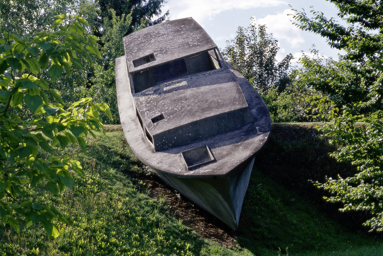 A concrete sculpture in the shape of a real boat appears to float on the hilly landscape o f the sculpture park.