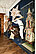 Photo of an exhibition room. On a long pedestal are various dressed up figures. One figure (Glöckler) wears a 1m high star on his head and shoulders. Another figure (Thomashutze) crouches on the floor and is covered with furs, only a red long beak can be seen.