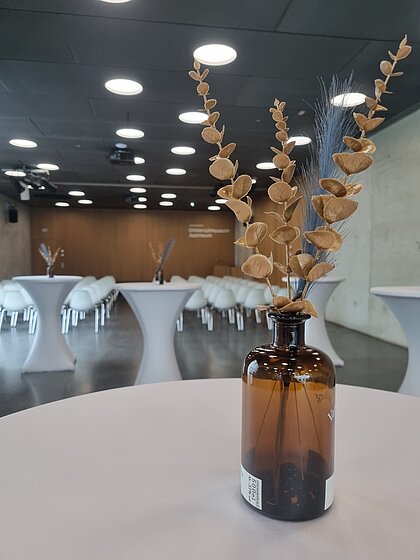 In the Auditorium in the Joanneumsviertel, chairs are set up in the background towards the stage. In the foreground are standing tables with decorations.