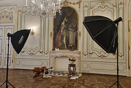 A photo shoot scenario with old books, candles and other objects is set up in front of the mural in Prunkraum 207. Two large spotlights are set up in the foreground.
