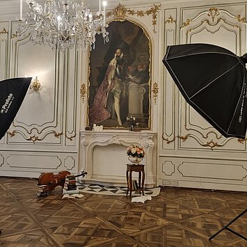 A photo shoot scenario with old books, candles and other objects is set up in front of the mural in Prunkraum 207. Two large spotlights are set up in the foreground.