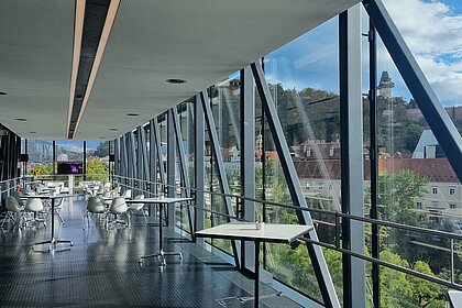 In der Needle im Kunsthaus Graz stehen im Vordergrund Stehtische. Im Hintergrund sind kleine Kaffeehaus-Sitzgruppen aufgestellt.