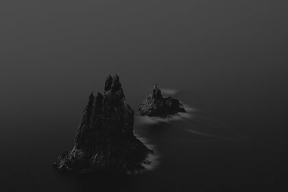 ein schwarz-weoß Bild, welches eine dunkle Felslandschaft im Ozean zeigt.