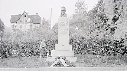 Ein Junge sieht zur Büste Roseggers hoch und hält ein Stück Brot in der rechten Hand. Ein Kranz liegt am Fuß des Rosegger-Brunnens.