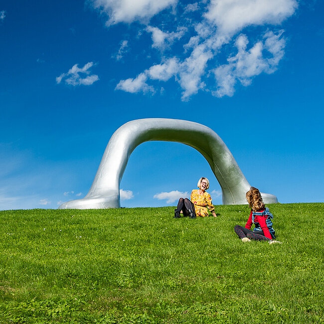 Ein Mutter genießt mit Kind den Sommertag im Österreichischen Skulpturenpark. Stark Präsent ist Peter Weibels Skulptur "Die Erdkugel als Koffer" 2004.