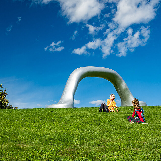 Ein Mutter genießt mit Kind den Sommertag im Österreichischen Skulpturenpark. Stark Präsent ist Peter Weibels Skulptur "Die Erdkugel als Koffer" 2004.