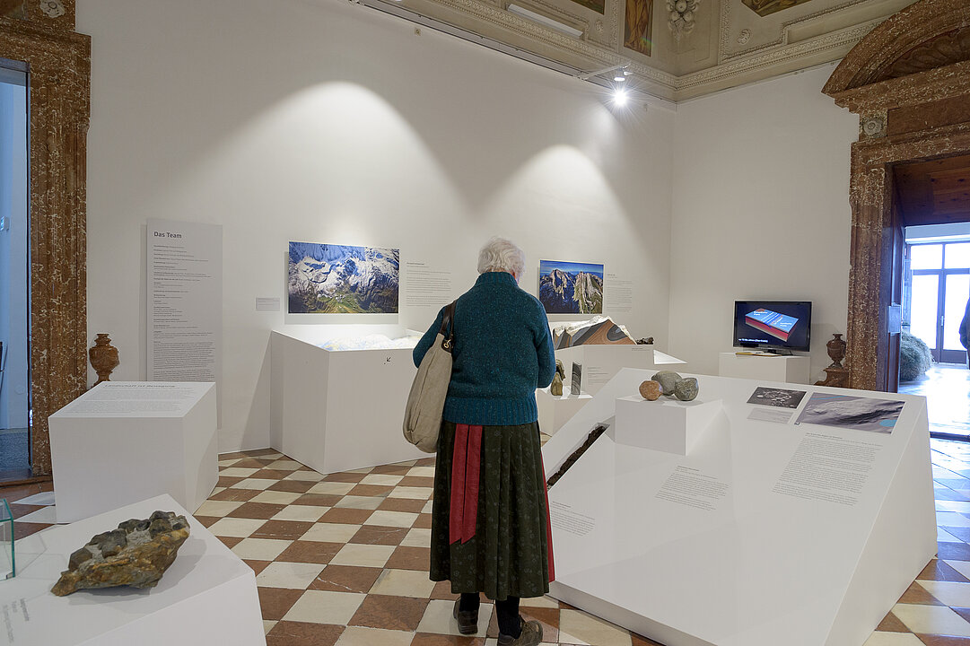 Eine Frau in Tracht steht in einem Ausstellungsraum und liest einen Text.