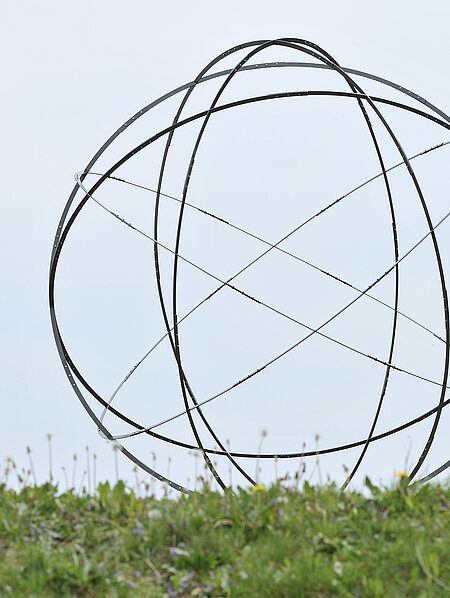 A sphere made of six metal circles rises from an earth pyramid above the water lily pond. It is one four-millionth of the earth. 