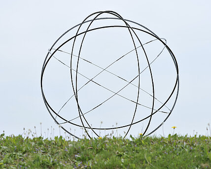 A sphere made of six metal circles rises from an earth pyramid above the water lily pond. It is one four-millionth of the earth. 