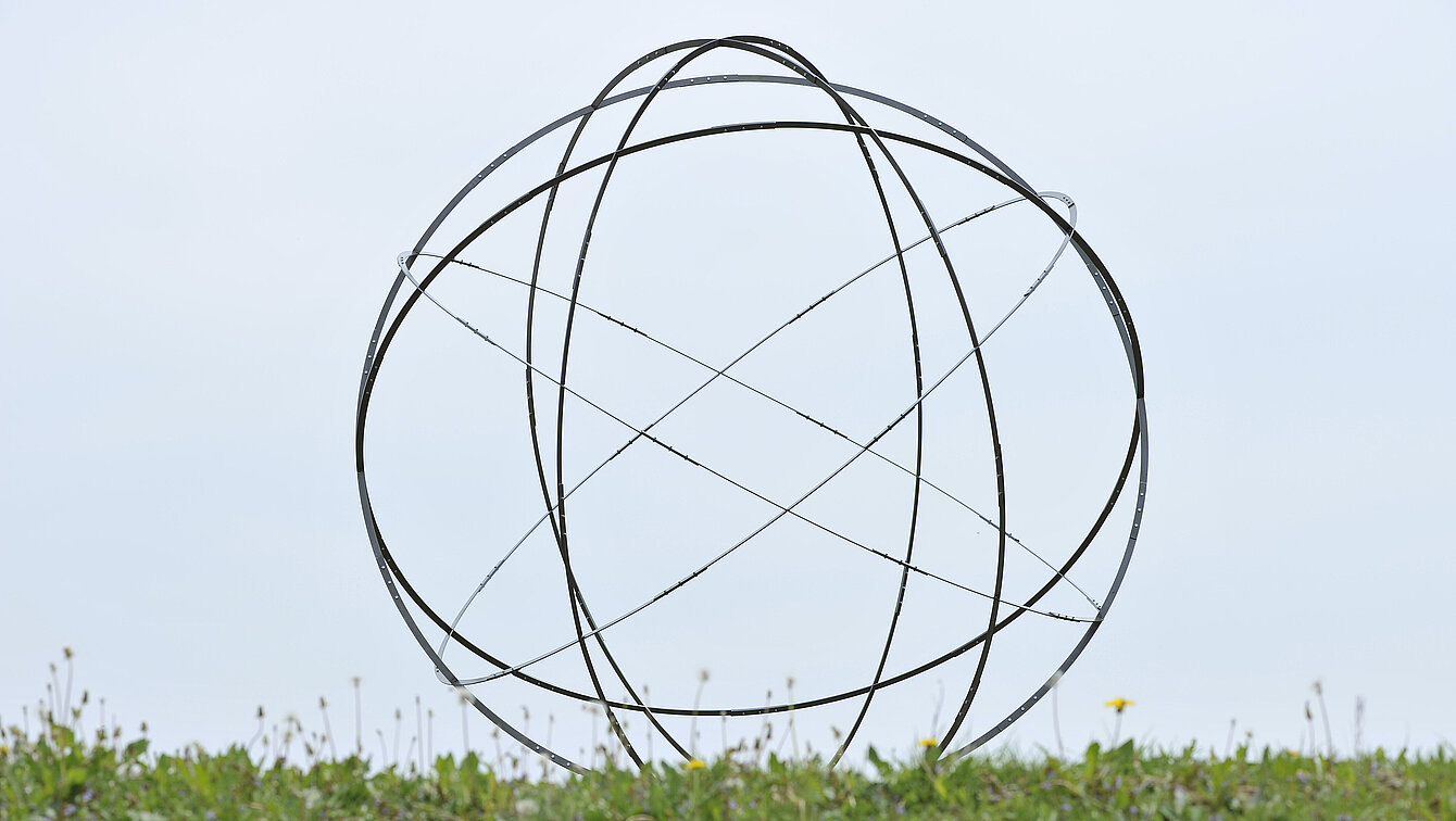 A sphere made of six metal circles rises from an earth pyramid above the water lily pond. It is one four-millionth of the earth. 