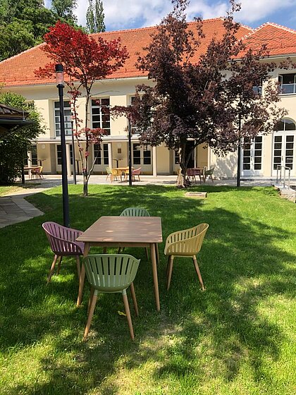 Blick Richtung Heimatsaal im Duftgarten. Im Vordergrund ist ein Tisch mit Sesseln, seitlich sieht man den Pavillon.