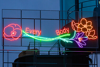Neoninstallation mit leuchtenden Blumen (Mohn, Narzissen, Krokusse) und dem Schriftzug "Every Body" an der Fassade des Kunsthauses Graz.