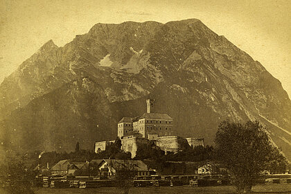 Alte Fotografie von Schloss Trautenfels. Das Schloss steht vor dem Berg Grimming. Das Foto ist gelb eingefärbt.