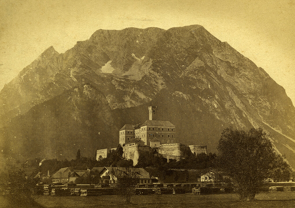 Alte Fotografie von Schloss Trautenfels. Das Schloss steht vor dem Berg Grimming. Das Foto ist gelb eingefärbt.