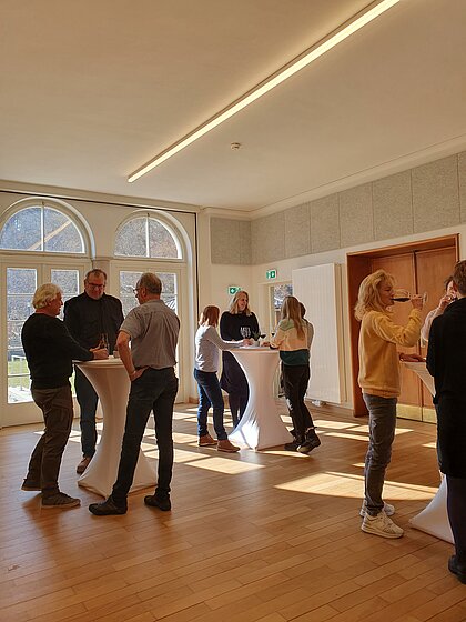 People stand at high tables in the foyer of the Heimatsaal during a reception.