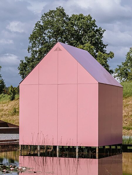 Am Seerosenteich neben dem Berggartencafé steht ein kleines rosa Einfamilienhaus. Über einen Steg zugänglich können drei Projektionen im Inneren begutachtet werden. 