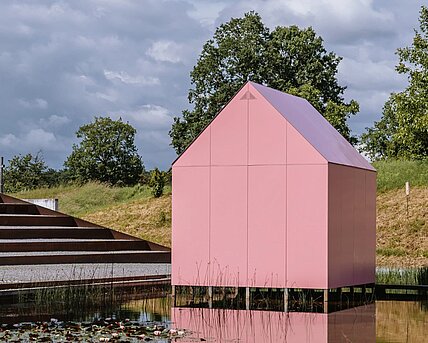 Am Seerosenteich neben dem Berggartencafé steht ein kleines rosa Einfamilienhaus. Über einen Steg zugänglich können drei Projektionen im Inneren begutachtet werden. 