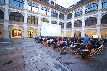 Im Lesliehof findet das Open Air Sommerkino statt. Besucher*innen sitzen vor der großen Leinwand.