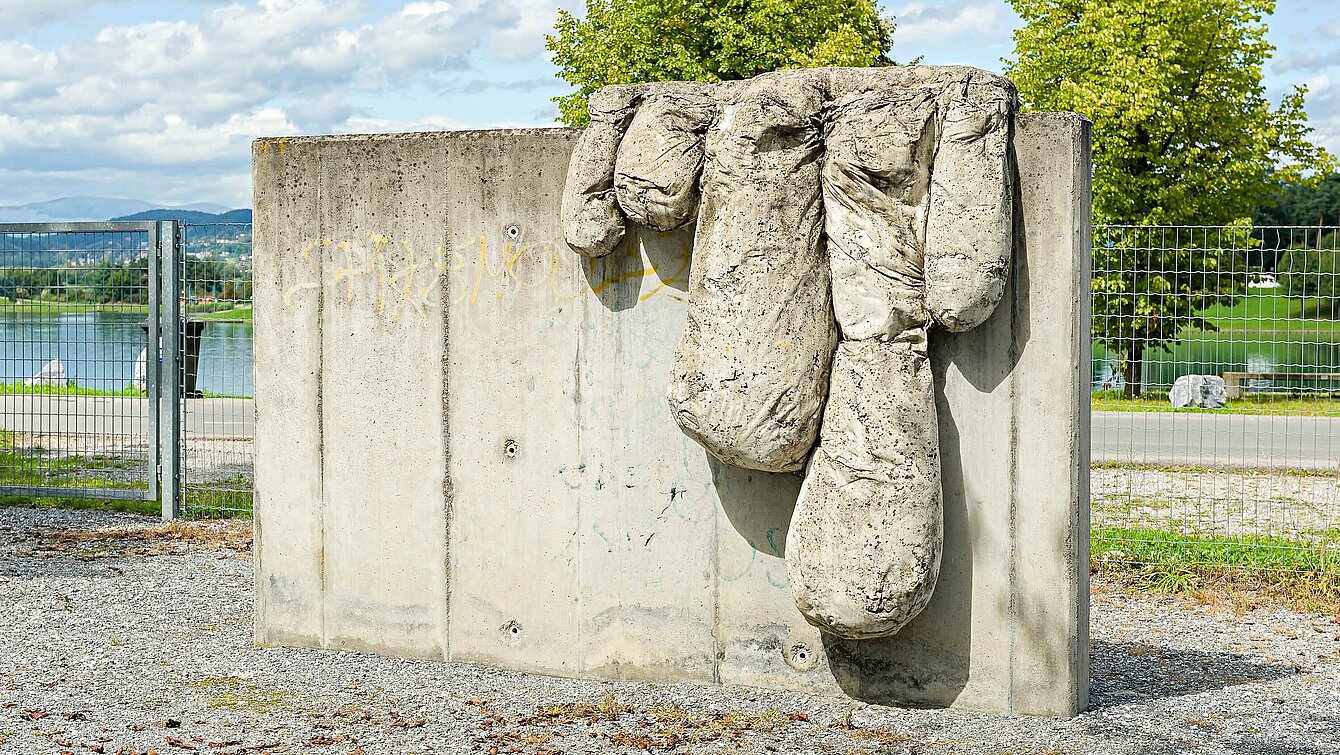 Die Skulptur des Malers Bohatsch ist eine senkrechte, glatte Betonplatte mit herabhängenden "Tropfen" aus Beton. Diese ähneln Fingern und sollen das langsam über die Leinwand kriechende Rinnen der Farbe simulieren.