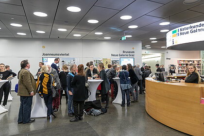 Menschen stehen an Stehtischen bei einem Empfang im Foyer im Joanneumsviertel.