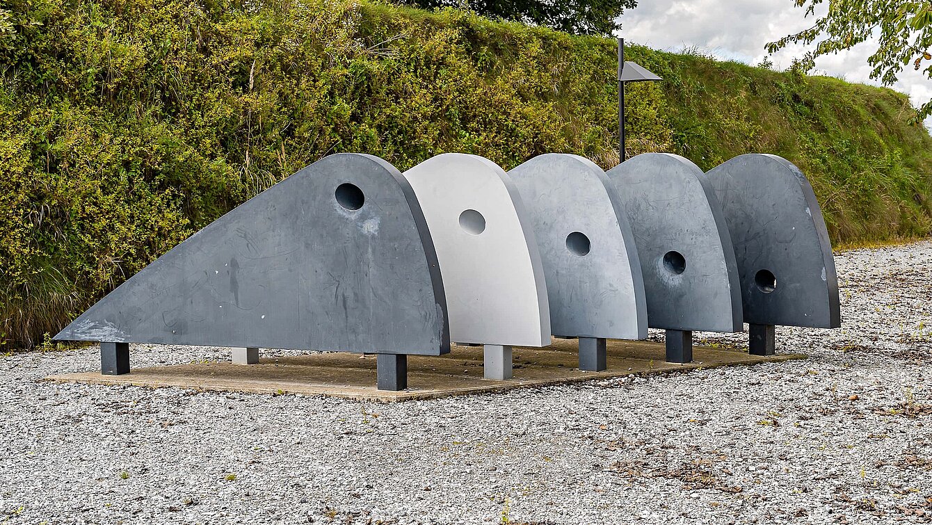 The "walking machine" by Karin Hazelwander consists of five winged elements in different shades of gray. It looks as if it could start moving at any time. The hole in each element shifts from the upper edge of the first curve to the lower edge of the fifth and last, suggesting an imaginary movement.