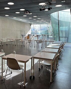 Tische mit Sesseln sind in viereckiger Form im Auditorium angeordnet.