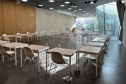 Tische mit Sesseln sind in viereckiger Form im Auditorium angeordnet.