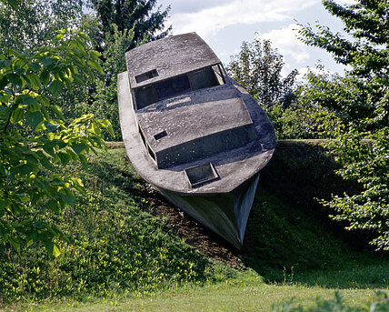 A concrete sculpture in the shape of a real boat appears to float on the hilly landscape o f the sculpture park.
