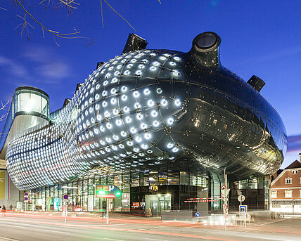 Ansicht des Kunsthaus Graz bei Nacht. Die BIX-Fassade leuchtet.