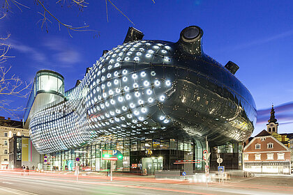 Ansicht des Kunsthaus Graz bei Nacht. Die BIX-Fassade leuchtet.
