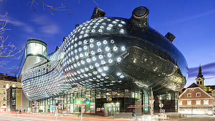 Ansicht des Kunsthaus Graz bei Nacht. Die BIX-Fassade leuchtet.