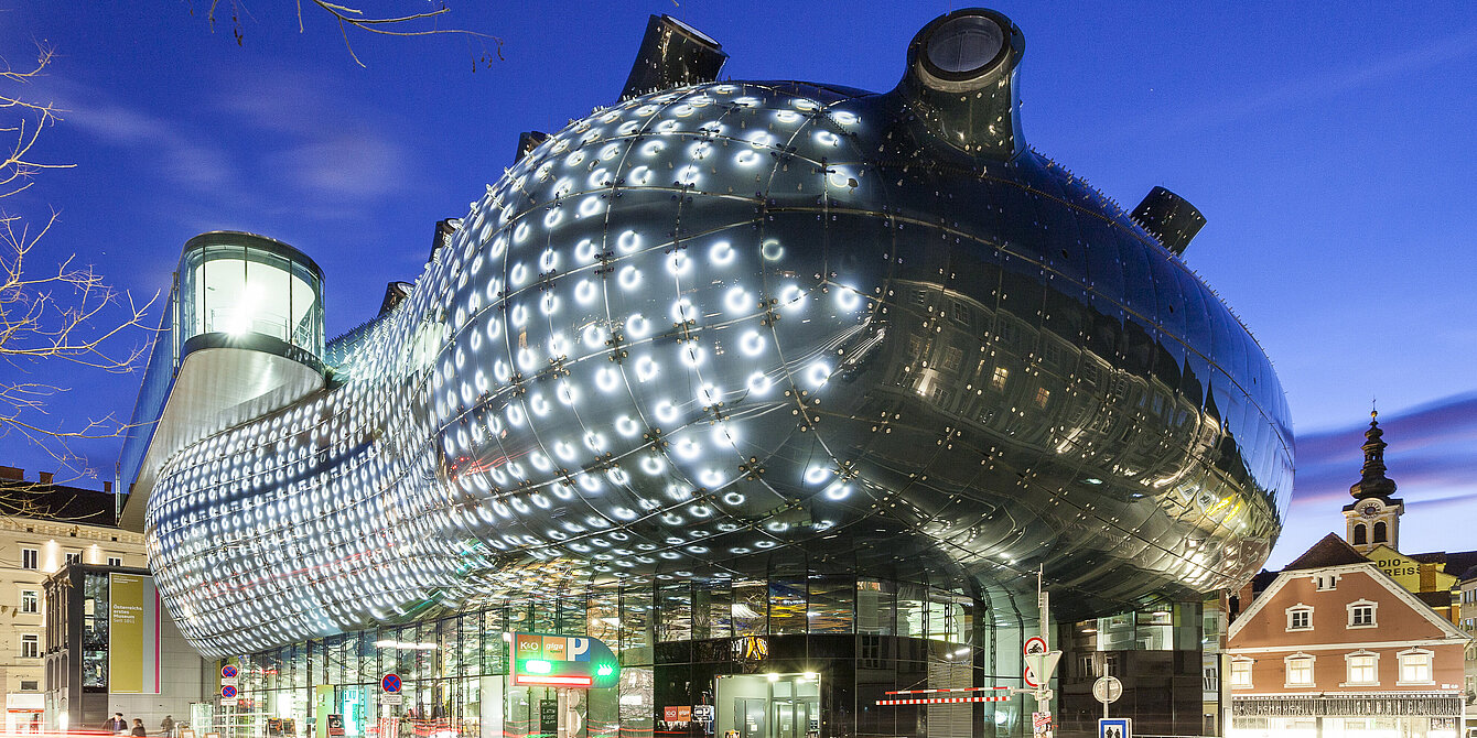 Ansicht des Kunsthaus Graz bei Nacht. Die BIX-Fassade leuchtet.