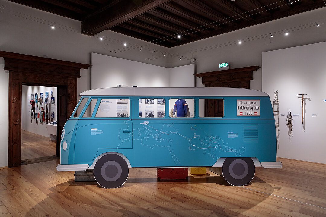 Ausstellungsansicht: In der Mitte des Raums steht ein grafischer Umriss von einem hellblauen VW-Bus.