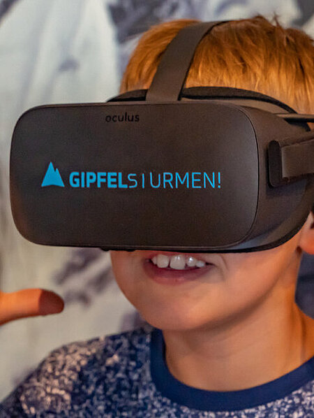 Ein Junge trägt eine schwarze VR-Brille mit der blauen Beschriftung Gipfelstürmen!