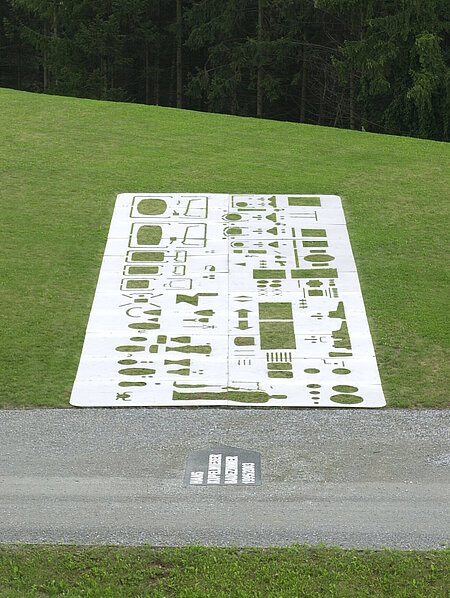 A steel plate with cut-out shapes is embedded in the way on a slope. The cut-outs are standardized symbols for elements in wet rooms. A human silhouette is also recognizable in Kupelwieser's bathroom.