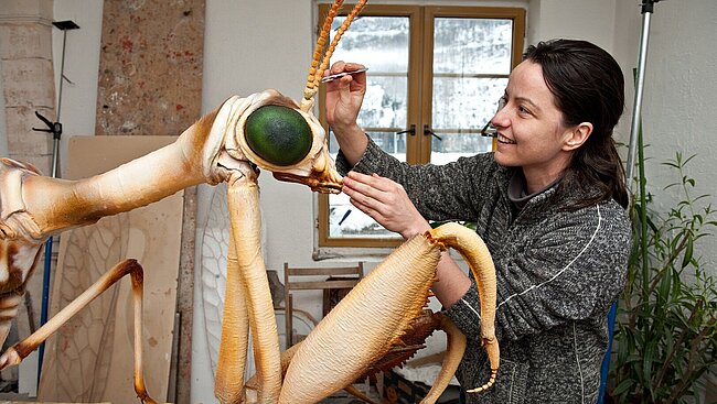 In ihrem Atelier steht die Künstlerin Mariya Tauschitz vor dem Modell des Steirischen Fanghaft und hält eine Pinzette nahe des stark vergrößerten Fühlers.