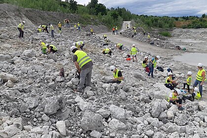 Personen unterschiedlichen Alters in gelben Warnwesten auf einem Geröllfeld des Steinbruchs, bei der Suche nach Fossilien.