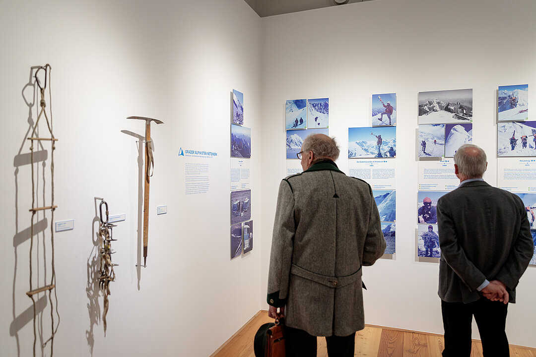 Foto von der Ausstellungseröffnung. Menschen stehen in einem Raum und betrachten Objekte.