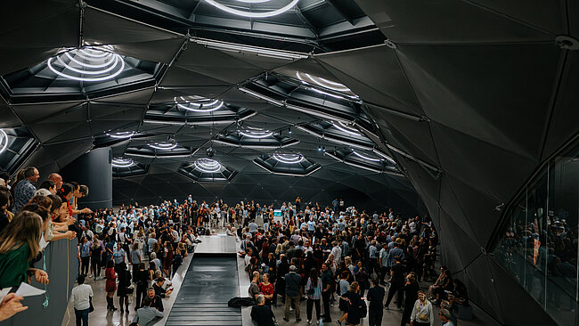 Anlässlich der Feierlichkeiten des 20-jährigen Jubiläums befinden sich zahlreiche Menschen im Ausstellungsraum Space01.