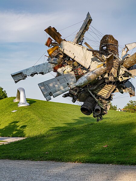 Blick vom Wegesrand auf die Skulptur "Airplane Parts & Hills" von Nancy Rubins und "Die Erdkugel als Koffer" von Peter Weibel in der Ferne