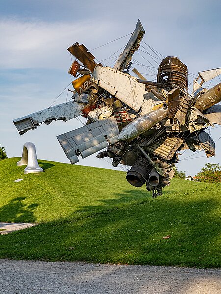 Blick vom Wegesrand auf die Skulptur "Airplane Parts & Hills" von Nancy Rubins und "Die Erdkugel als Koffer" von Peter Weibel in der Ferne