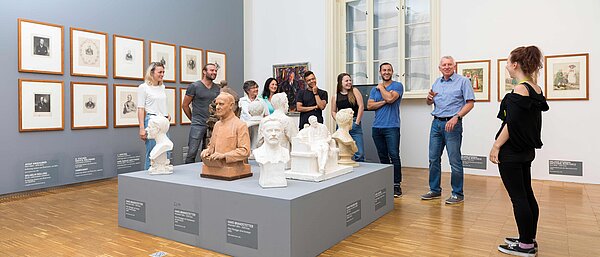 Eine Museumsmitarbeiterin führt eine Gruppe an Besucher:innen durch eine Ausstellung in der Neuen Galerie Graz.