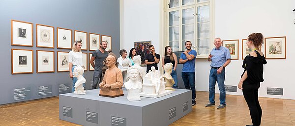 Eine Museumsmitarbeiterin führt eine Gruppe an Besucher:innen durch eine Ausstellung in der Neuen Galerie Graz.