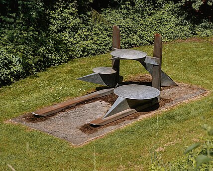 Das Zentrum der Skulptur bilden die beiden vertikalen und horizontalen Träger, auf die sich die Konstruktion stützt. Die Formen scheinen sich in einem fein ausbalancierten Gleichgewicht zu befinden und strahlen trotz der Schwere des Materials eine gewisse Leichtigkeit aus. Ihre konkrete Bedeutung gewinnt die Arbeit aus Vergleichen der einzelnen Bestandteile der Skulptur mit allgemein bekannten Objekten.